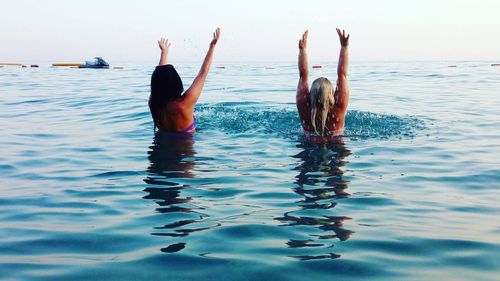 Rear view of women with arms raised at sea