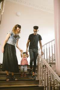 Full length of family moving down on staircase in apartment