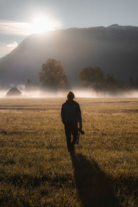 Silhouette of unrecognizable male traveler walking on grassy meadow near mountain ridge in misty morning in austria