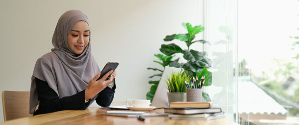 Young woman using mobile phone while sitting on table at home