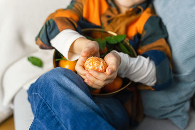 Close view of the hands of a child holding a tangerine. bright colors.