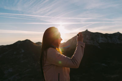 Woman standing on mountain against sky during sunset