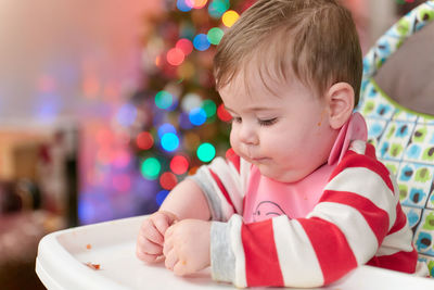 Little boy toddler eating in his high chair in front of the christmas tree