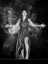 Portrait of young woman with arms outstretched standing against plants