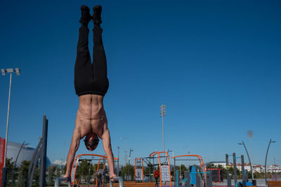 Low angle view of woman exercising against clear blue sky