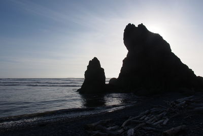 Silhouette rock formation at beach against sky during sunset