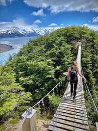 Woman standing on footbridge against mountain