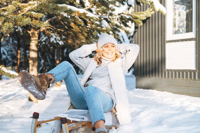 Portrait of smiling young woman sitting on snow covered field