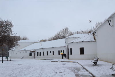 Snow covered houses by buildings against sky