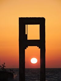 Silhouette built structure by sea against orange sky