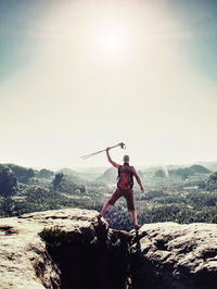 Man hiker raised arm with stick. happy tourist guide on the sharp summit in sunny day.