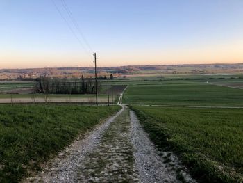 Road amidst field against sky during sunset