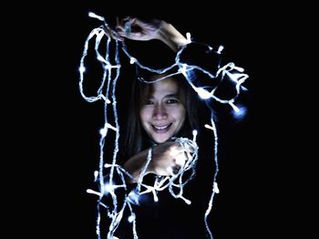 Portrait of woman holding christmas lights against black background