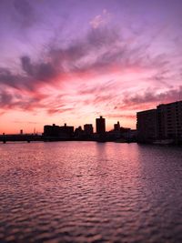 Sea by buildings against sky during sunset