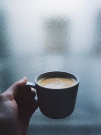 Cropped image of hand holding coffee cup against frosted glass