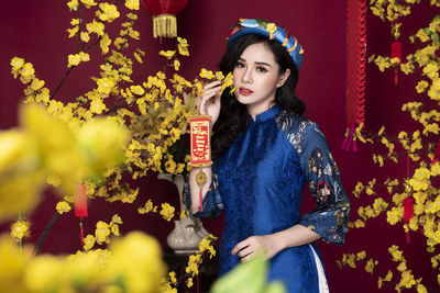 Young woman looking away while standing against yellow flowering plants
