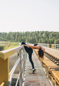 Full length of woman exercising on railway bridge against sky
