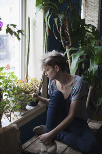 Woman sitting by potted plant against window