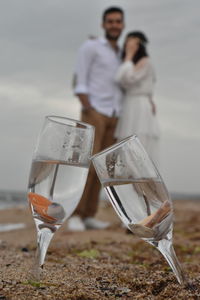 Midsection of couple standing on beach against sky