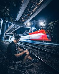 Young man sitting by railroad track at night