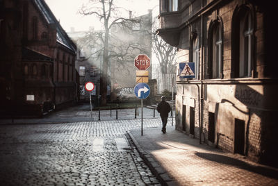 Rear view of man walking by road signs on sidewalk in city