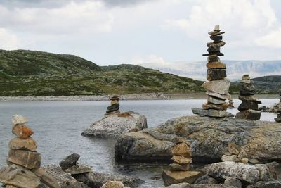 Stack of stones on rock by river against sky
