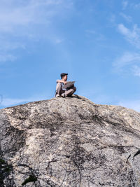 Man sitting on rock against sky