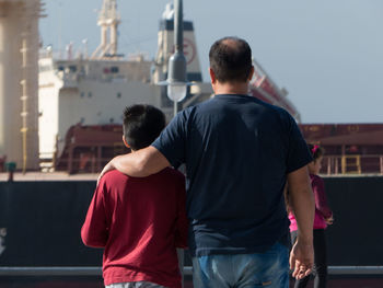 Rear view of people standing against ship and sky