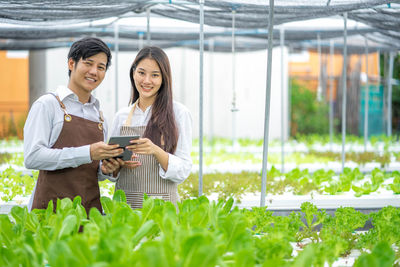 Portrait of young woman using mobile phone while standing in greenhouse