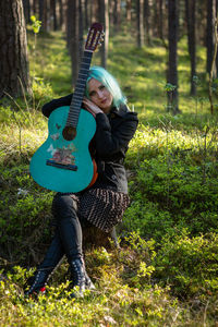 Hipster young woman with turquoise guitar sitting in forest