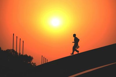 Low angle view of silhouette woman walking on street against sky during sunset