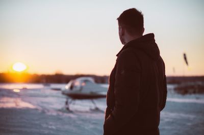 Man standing at beach against sky during sunset