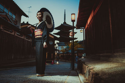 Side view of woman standing on footpath amidst buildings in city