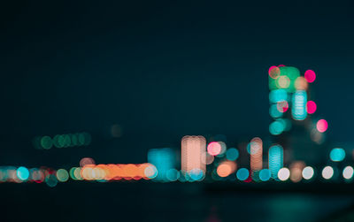 Defocused image of illuminated lights in city against sky at night