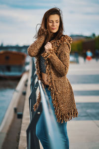 Beautiful woman with hand in hair standing by railing