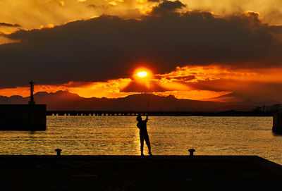 Silhouette people standing by sea against sky during sunset