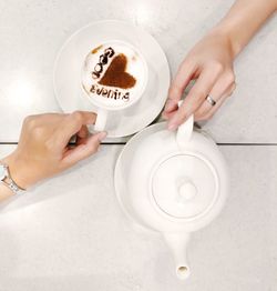 Coffee or tea. one hand is holding a cup of cappuccino and other hand is holding a tea pot.