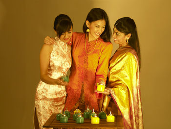 Smiling young friends with oil lamps against wall