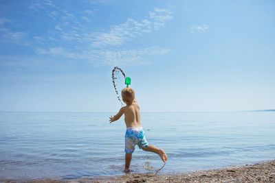 Full length of shirtless boy playing on beach against sky