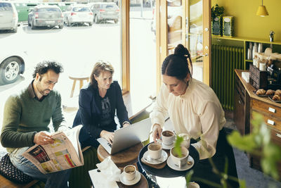 High angle view of waitress picking up coffee cups while customers sitting at table