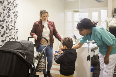 Pediatrician giving stickers to boy while mother standing with baby stroller in hospital