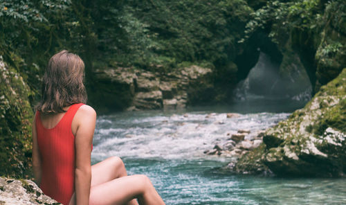 Rear view of woman sitting on rock by sea