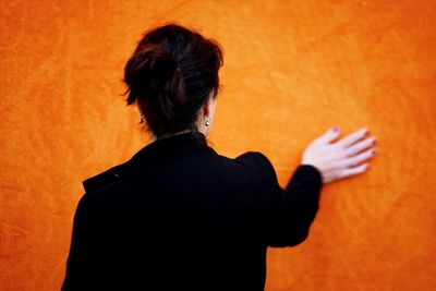 Rear view of silhouette woman standing against orange wall