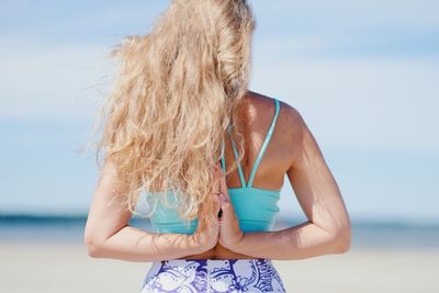 Girl standing at the beach in a yoga pose, facing the sea with wind blowing her hair