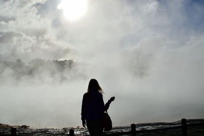 Silhouette of woman standing on landscape against cloudy sky