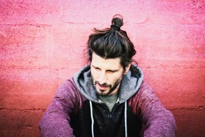 Close-up of thoughtful young man sitting by wall