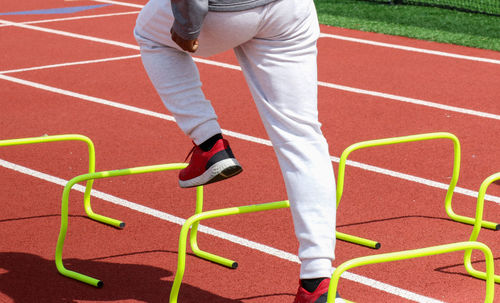 Rear view of a high school boy standing over yellow hurdles on a track doing sports training drills.