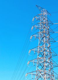 Low angle view of electricity pylon against clear blue sky