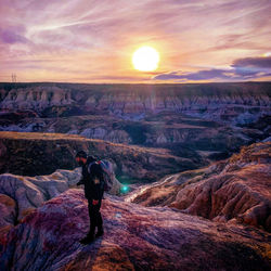 Full length of man standing on rock against sky during sunset