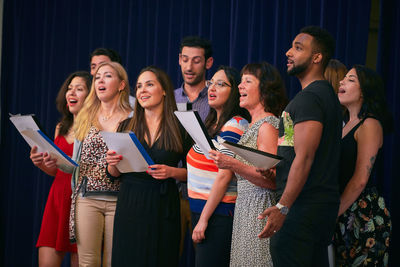 Male and female friends holding music sheets rehearsing on stage